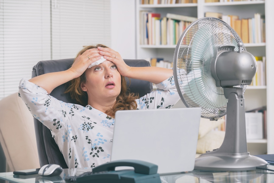 Woman suffers from heat while working and tries to cool off by the fan due to broken air conditioning in home