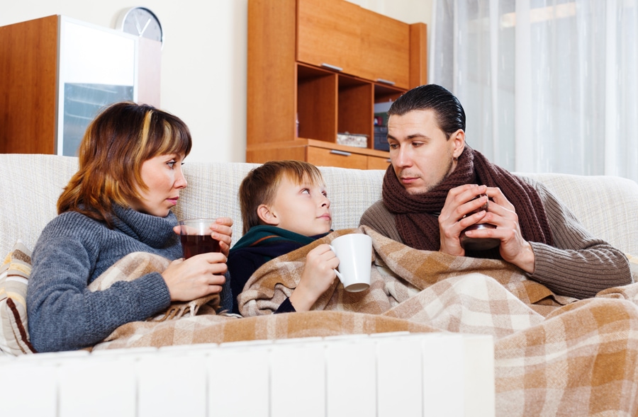 Family snuggled on couch with blanket trying to stay warm and decide if it's time to buy a new furnace.