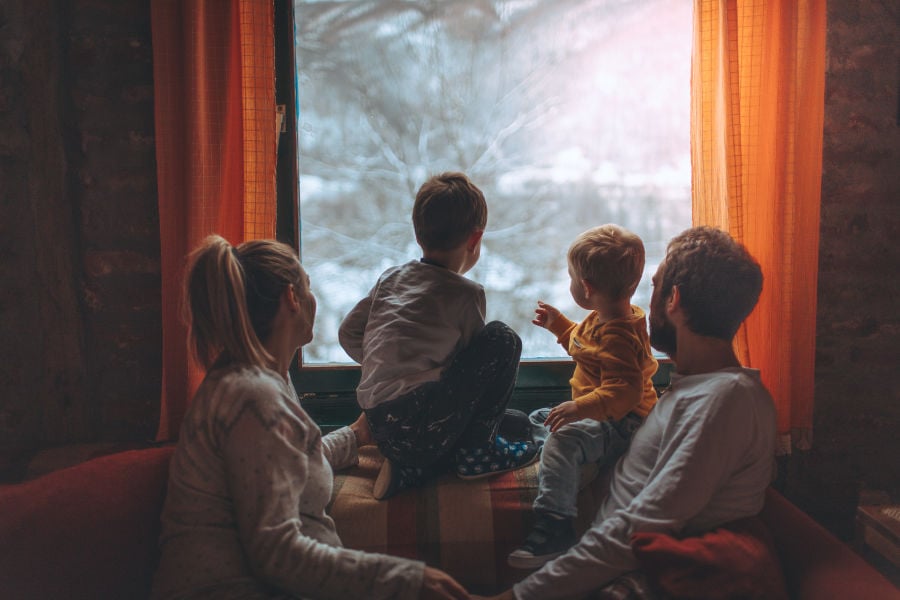 Family looking out their living room window in winter after learning how to keep their heat in extreme cold weather.