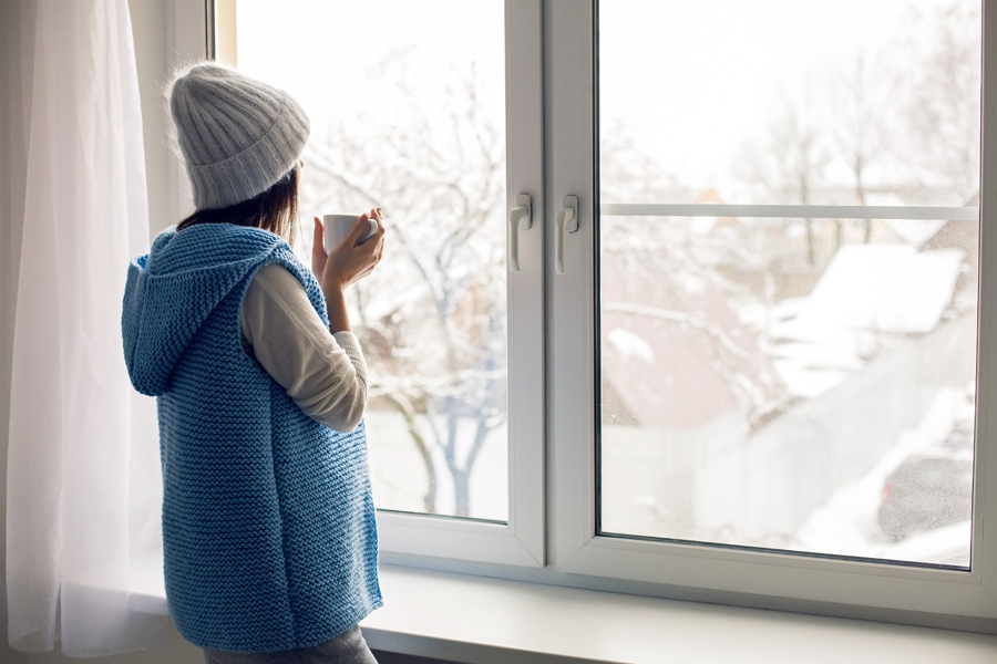 Woman looking out window in winter time trying to figure out how she can make her furnace last longer.